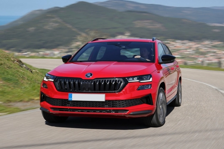 A red Skoda Karoq driving along a scenic road.